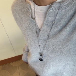 Long collier argenté avec pendentif cœur noir et perle tachetée sur un pull gris chic