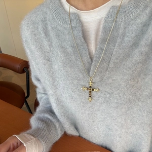 Detail van vintage gouden kruis ketting met tijgeroog stenen op een gebreide trui