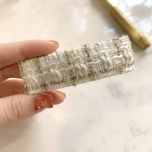 Detailed macro of white and gold tweed fabric texture on an elegant rectangular hair clip