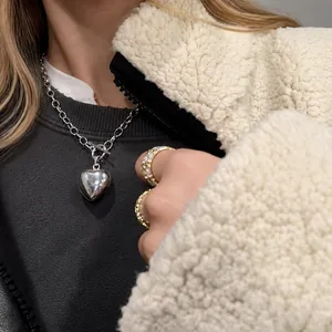 Primer plano de collar con colgante de corazón de acero de titanio y anillos de moda