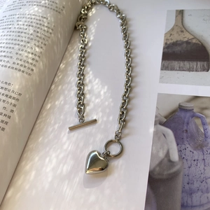 Detalle de collar de corazón plateado con cierre de barra OT y cadena de acero gruesa