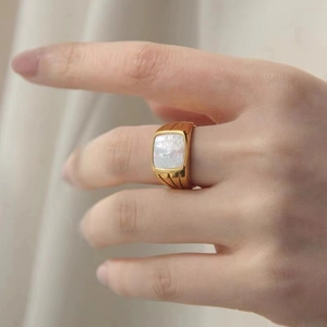 Detail view of a gold-plated signet ring featuring a square shell inlay and striped texture