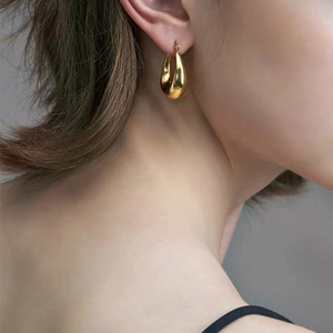 Polished gold plated oval U-shaped drop earrings for women worn by a model