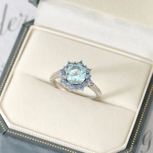Light blue round halo ring with small dark blue diamonds in a luxury jewelry gift box
