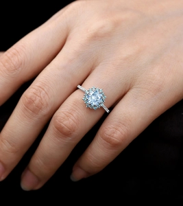 Macro shot of light blue round gemstone ring with floral diamond halo on model's hand