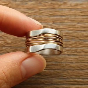 Macro shot of wide wave-shaped dual-tone ring with intricate gold wire wrap detail