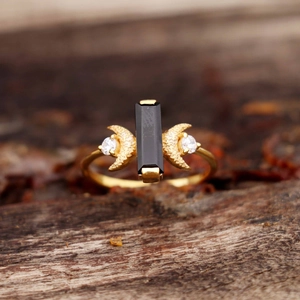 Bague dorée en forme de lune avec pierre noire et détails en zircone sur fond bois naturel