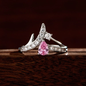 Silberner Kreuzring mit rosa Saphir im Birnenschliff und Diamanten auf Holzgrund