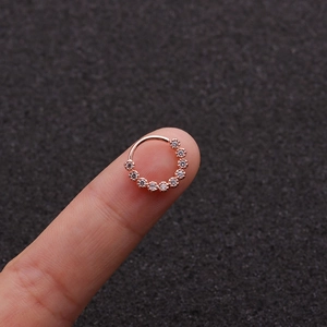 Vue macro d'un anneau de nez en or rose avec zircons micro-pavés tenu sur un doigt