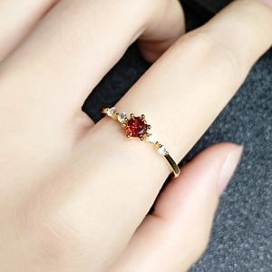 Close-up of a 18K gold ruby ring with side diamonds on a finger against a dark background