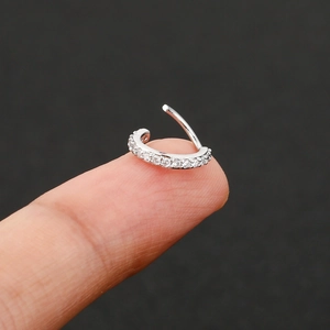 Silver cartilage piercing hoop with cubic zirconia pave inlay shown on fingertip
