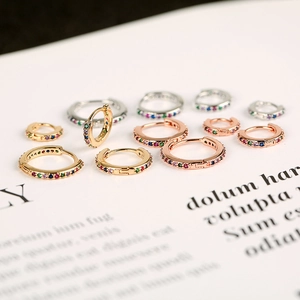 Dettaglio di orecchini huggie con zirconi arcobaleno in finiture oro, argento e oro rosa