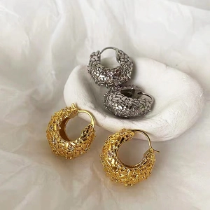Detail van gevlochten oorringen in goud en zilver met glinsterende zirkonia-stenen