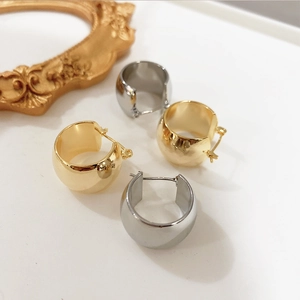 Détail de boucles d'oreilles créoles C épaisses en or et argent sur une surface minimaliste