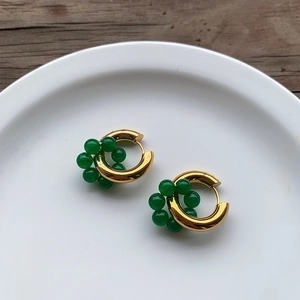 Macro detail of retro gold hoop earrings with emerald green beads on a white plate