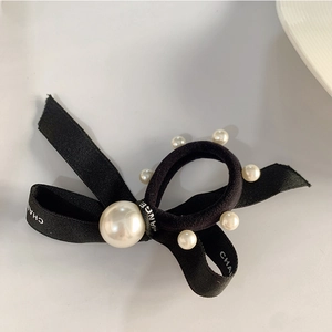 Détail du chouchou noir avec nœud, perles élégantes et texture de ruban avec logo imprimé