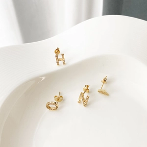 Macro shot of gold-plated letter earrings with inlaid cubic zirconia on white ceramic