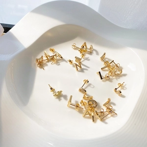 Detailed macro shot of gold letter earrings with micro-inlaid zircons on ceramic plate