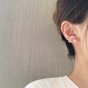 Close-up of asymmetric gold letters O and W earrings with micro-inlaid zircons on ear
