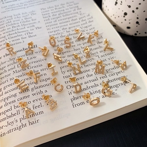 Macro shot of 26 gold letter stud earrings with pave zircon on vintage book pages