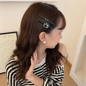 Close-up of matte black hair clips with white Smile text and smiley face on wavy brown hair