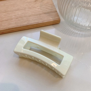 Close-up of a glossy cream-colored large square hair claw clip on a minimalist wooden tray