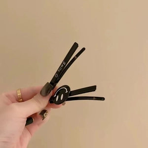 Detail of two black metal smile hair clips showing the duckbill design and matte finish