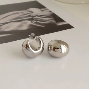 Detailopname van gepolijste metalen bolvormige oorbellen op een witte ondergrond
