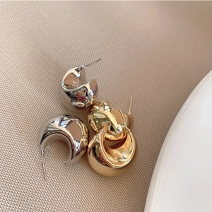 Detail van dikke minimalistische gouden en zilveren oorringen op een beige getextureerde stof
