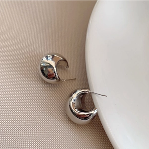 Detailopname van dikke zilveren oorringen met een gepolijste spiegelafwerking op stof