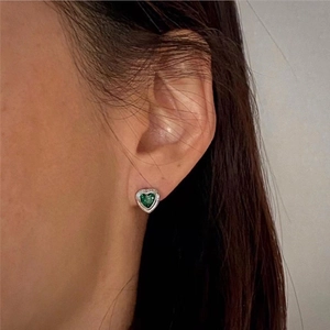 Minimalistischer silberner Ohrstecker mit grünem Herz-Zirkon am Ohr eines Damenmodels