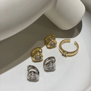 Detailaufnahme von Herz-Zirkon-Ohrringen und Kordelring auf minimalistischen weißen Ständern