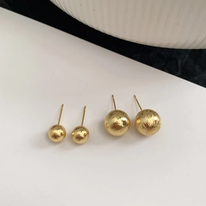 Detail of two pairs of minimalist gold spherical stud earrings with brushed metal finish