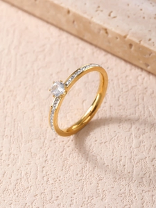 Dettaglio di un anello dorato a sei griffe con pietra rotonda e piccoli diamanti