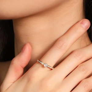 Squisito anello solitario a sei griffe dorato con diamanti laterali sulla mano della modella