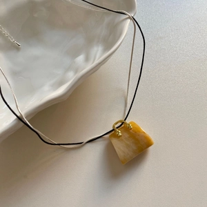 Dettaglio di un ciondolo in ambra a forma di borsa su cordino nero e catena d'argento