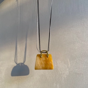 Dettaglio di pendente a borsa in pietra con manico dorato e ombre su muro grigio