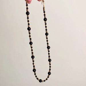 Dettaglio della collana con occhio di tigre, onice nero e perline dorate con chiusura in metallo