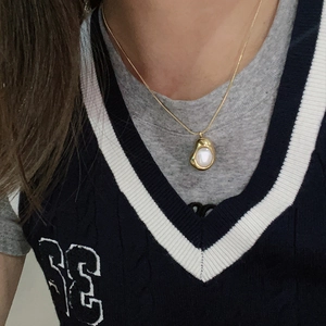 Detalle de un collar dorado minimalista con colgante orgánico e incrustaciones de nácar blanco