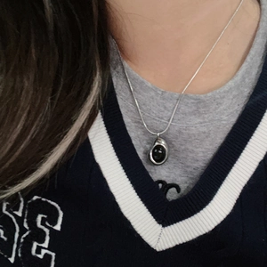 Detalle de collar de acero de titanio plateado con colgante ovalado negro en una modelo
