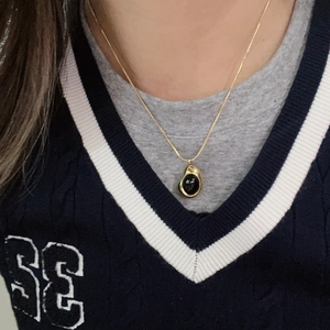 Primer plano de un collar dorado con un colgante irregular de piedra de ónice negro