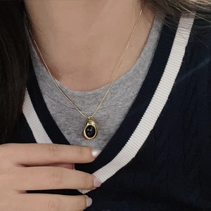 Primer plano de un collar dorado con colgante de gota de agua irregular usado por una modelo