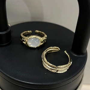 Detail of gold-plated feather ring and white cat-eye stone ring on a black surface