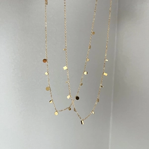 Detail einer minimalistischen vergoldeten Kette mit kleinen geometrischen Plättchen