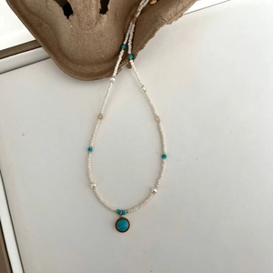 Detail of freshwater pearl necklace with turquoise pendant and golden accents on beige pulp