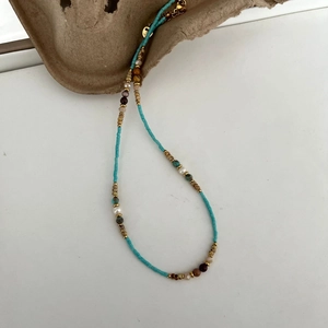 Macro detail of beaded necklace showing blue stones, pearls, and gold logo tag