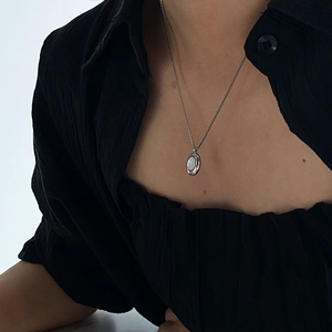 Detail of white shell oval pendant on a silver-tone chain worn with a black blouse