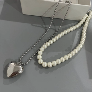 Detail of silver titanium heart pendant and white pearl necklace on grey background