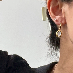 Close-up of elegant gold plated oval white shell pendant earrings worn by a model