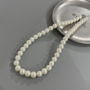 Detailed shot of white pearl necklace on a gray background with silver clasp details
